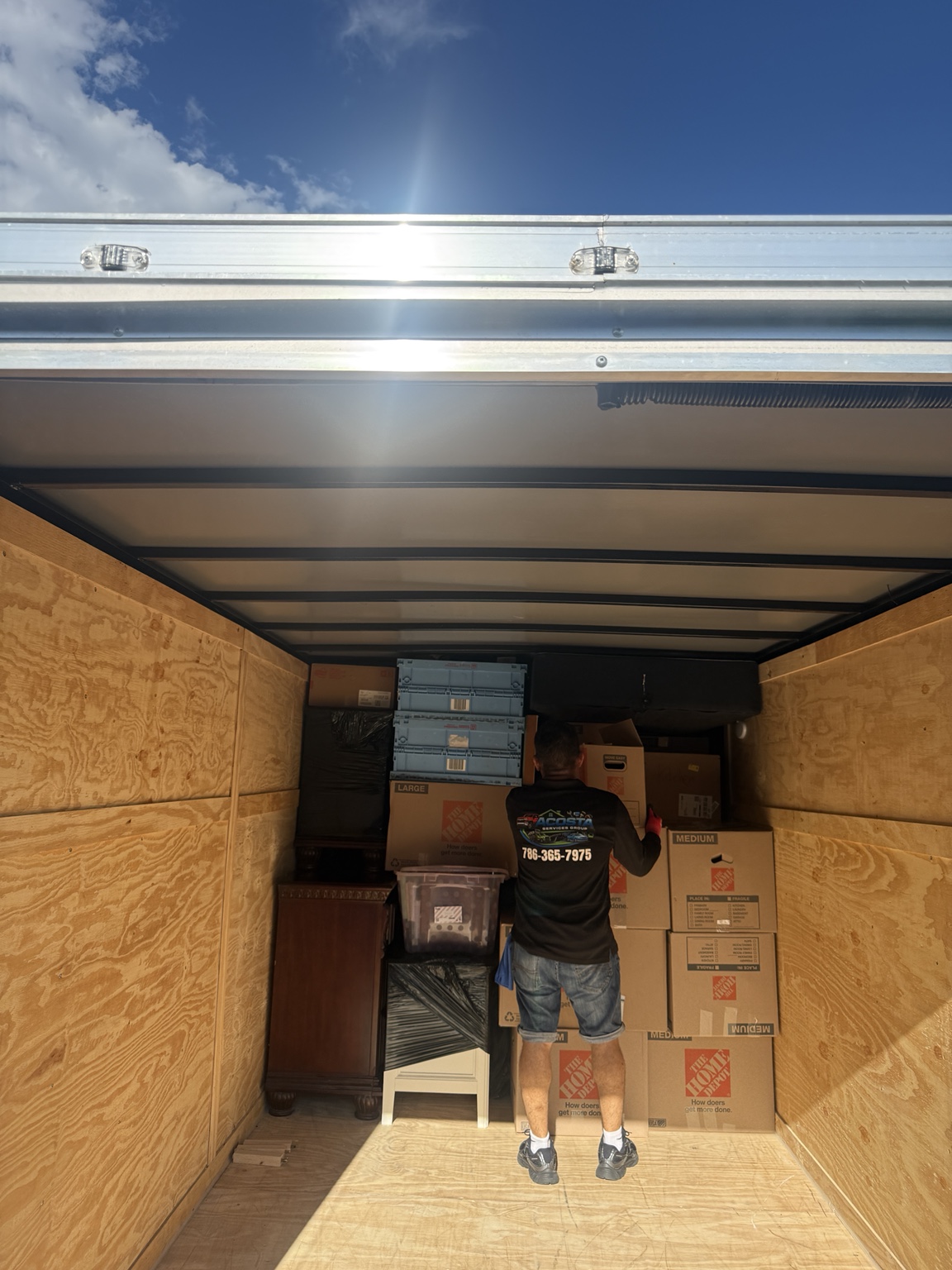 Acosta Services Group team member organizing boxes and household furniture inside an enclosed moving trailer